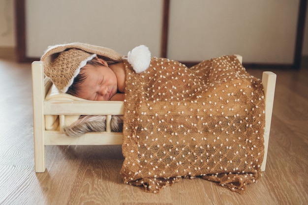 L'enfant est allongé sur un lit en bois sous une couverture. portrait d'un petit enfant dans un chapeau chaud avec un pompon.