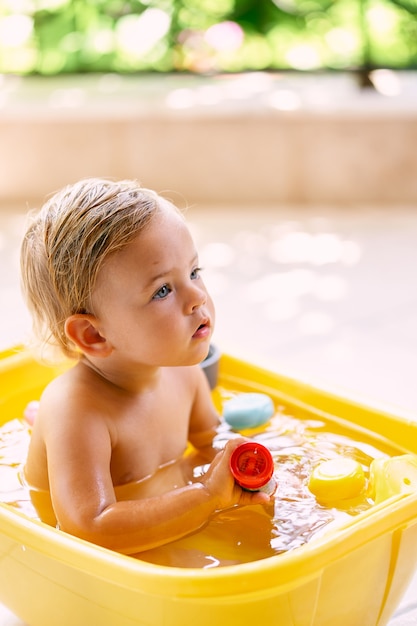 L'enfant est assis dans un bol d'eau et tient un jouet à la main