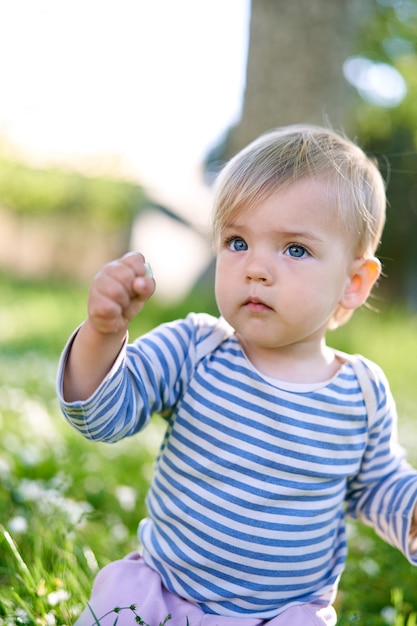 L'enfant est assis sur ses genoux avec son poing levé sur le portrait de la pelouse verte