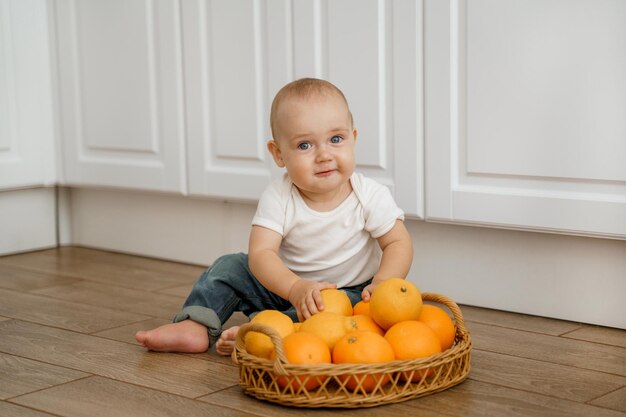 l'enfant est assis sur le sol de la cuisine avec un panier d'agrumes