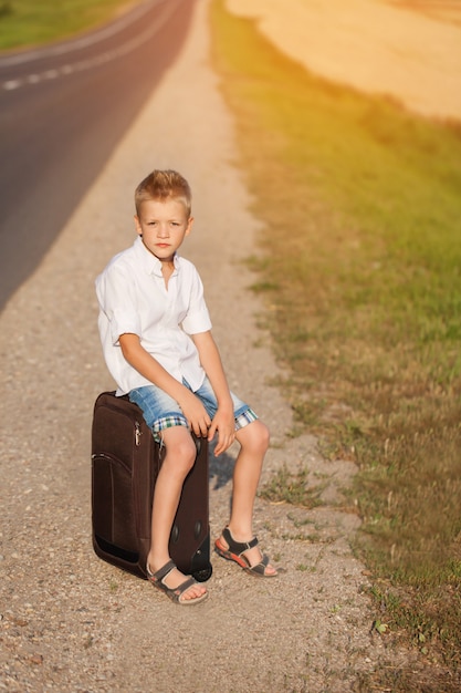 L&#39;enfant est assis sur une valise dans la journée ensoleillée d&#39;été, le voyageur