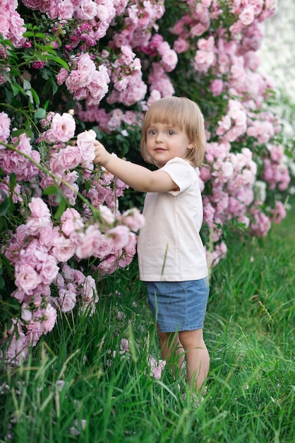 Photo un enfant est une fille vêtue d'une robe blanche sur fond de rosiers roses