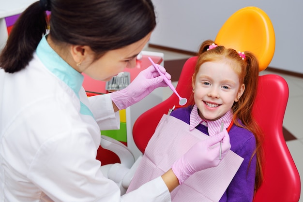 L'enfant est une petite fille rousse souriante assise dans un fauteuil dentaire. Dentisterie pédiatrique, dents de lait