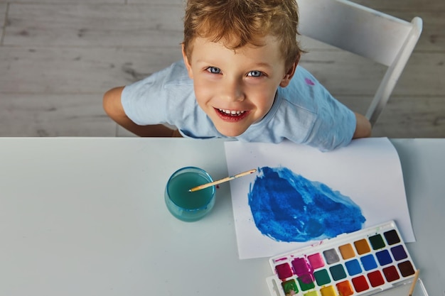 L'enfant est satisfait du dessin terminé réalisé avec un pinceau et de la peinture bleue