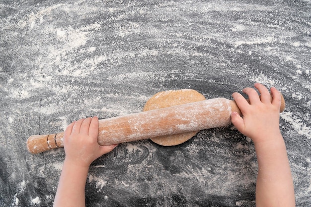 Enfant étalant la pâte sur la table à farine Vue de dessus