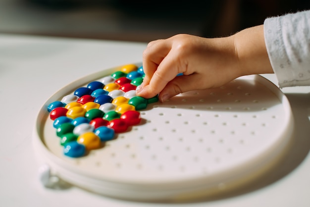 Un enfant étale une figure en mosaïque multicolore avec sa main.