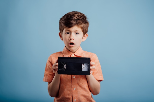 Enfant étonné avec une bande vidéo isolée sur fond bleu regarde la caméra