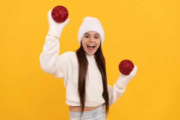 Un enfant étonné en chapeau d'hiver et des gants tiennent des boules de Noël décoratives sur fond jaune, nouvel an.