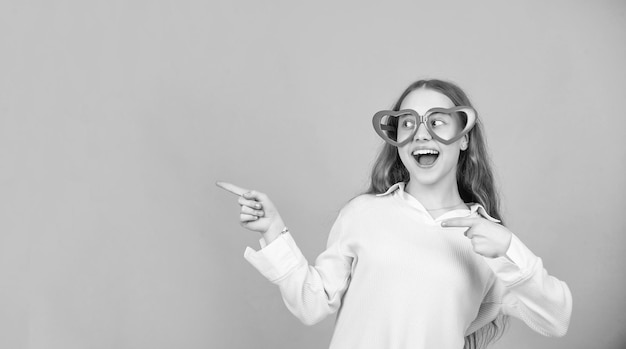 Enfant étonné dans des lunettes de fête pointant le doigt sur fond bleu avec accessoire de mode espace copie