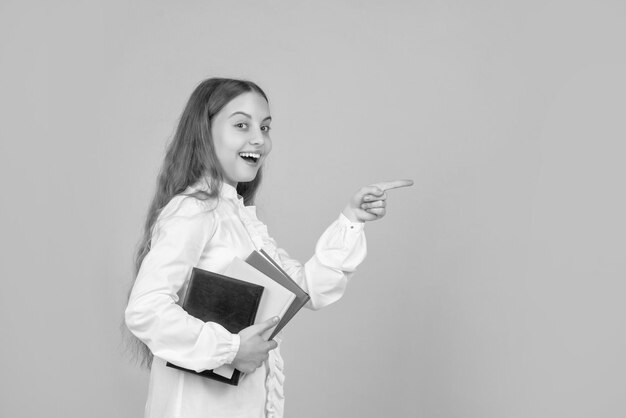 Enfant étonné avec le doigt pointé du livre sur l'espace de copie retour à l'école journée de la connaissance de l'éducation de la petite enfance enfant tenir un élève de cahier au lycée adolescente faire ses devoirs avec un cahier