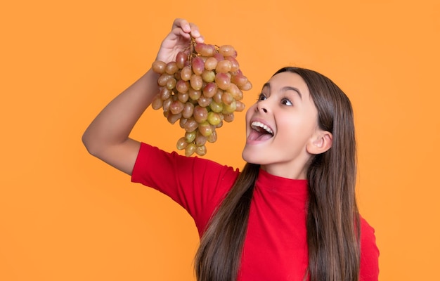 un enfant étonné mange un bouquet de raisins sur un fond jaune