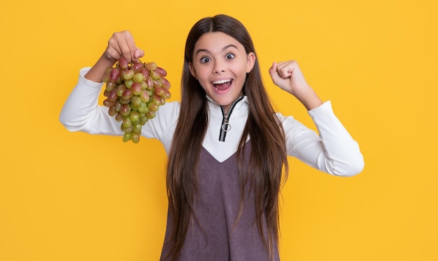 Enfant étonné surpris tenant des fruits de raisins frais sur fond jaune