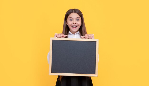 Un enfant étonné en uniforme tient le tableau noir de l'école pour la promotion de l'espace de copie