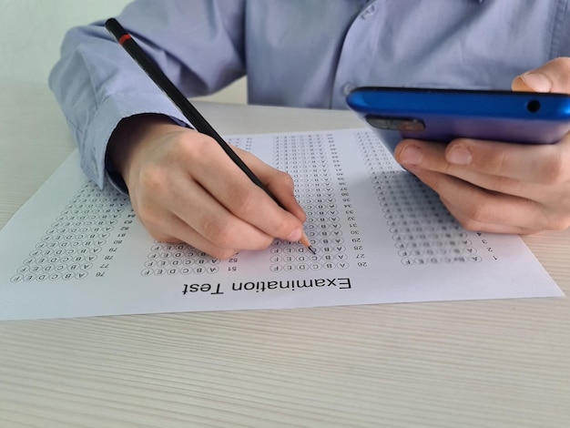 Enfant étudiant tenant un smartphone pendant le test d'examen de contrôle à l'école et trichant à l'examen