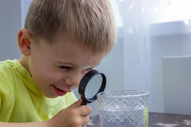 L'enfant examine l'eau avec une loupe dans un verre Mise au point sélective