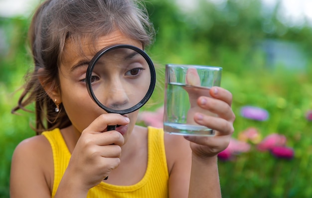 L'enfant examine un verre d'eau avec une loupe. Mise au point sélective.