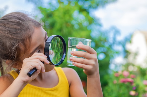 L'enfant examine un verre d'eau avec une loupe. Mise au point sélective.