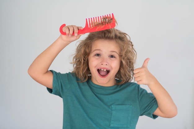 Enfant excité avec des cheveux blonds bouclés tenant une brosse à cheveux en peigne pour peigner un petit enfant garçon peignant hai