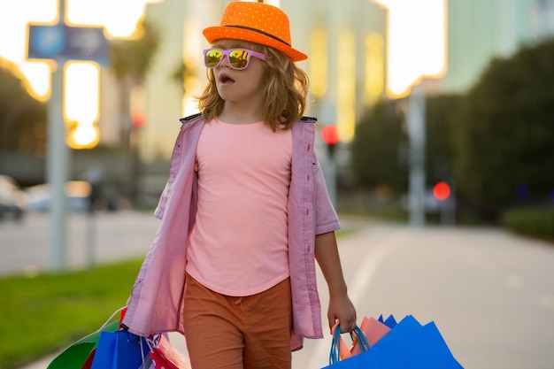 Un enfant excité dans des vêtements de mode va faire du shopping un enfant étonné avec des forfaits d'achat