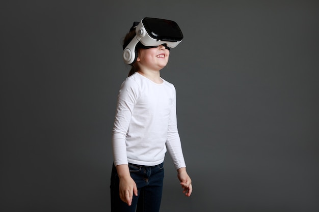 Enfant faisant l'expérience de la réalité virtuelle sur une surface grise. Surpris jolie fille à la recherche de lunettes VR.