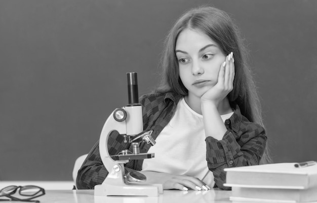 Enfant fatigué avec microscope en classe à la biologie du tableau noir