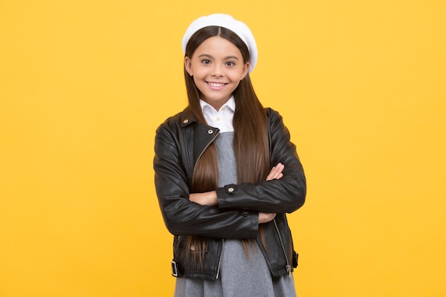 Enfant de fille d'âge scolaire confiant sourire heureux gardant les bras croisés fond jaune, confiance.