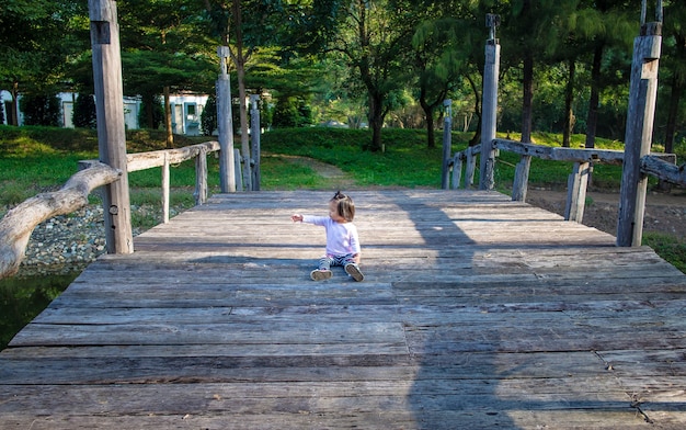 enfant fille assise et doigt pointant sur le pont en bois