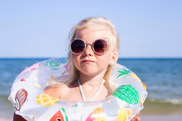 Enfant fille blonde à lunettes de soleil avec un anneau en caoutchouc sur la plage