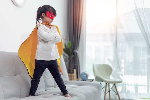 Enfant fille en costume de super héros avec masque et cape rouge à la maison