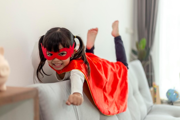 Enfant fille en costume de super héros avec masque et cape rouge à la maison