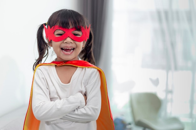 Enfant fille en costume de super héros avec masque et cape rouge à la maison