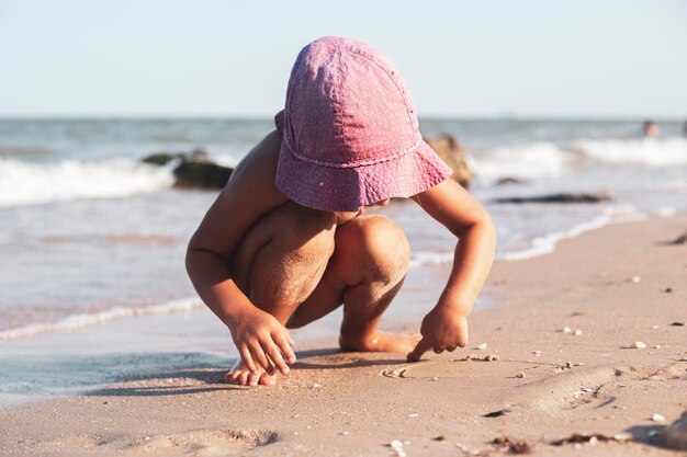 Enfant fille dans un chapeau panama rose s'appuie sur le sable sur la plage.