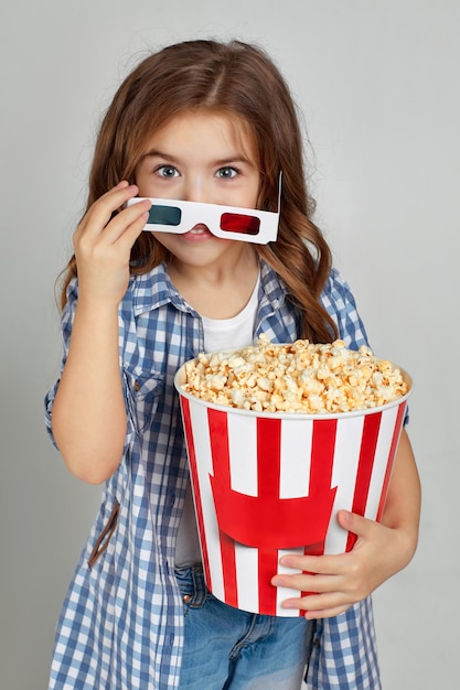 Enfant fille dans des lunettes 3d bleu rouge tenant un seau de pop-corn
