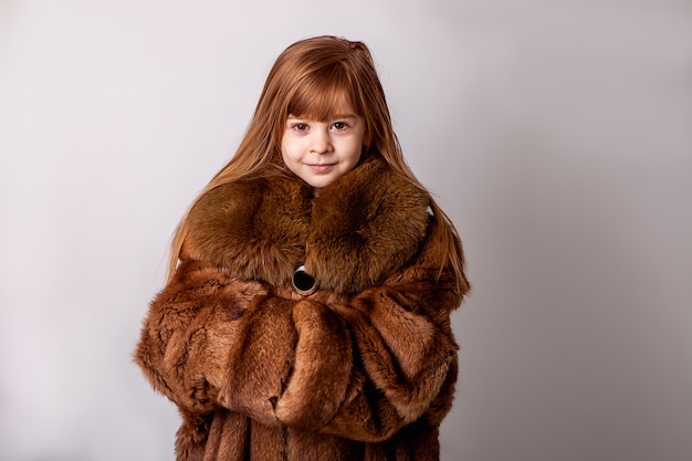 Un enfant, une fille dans le manteau de fourrure de sa mère. Fausse fourrure, vêtements d'hiver, manteaux de fourrure grande taille pour enfant