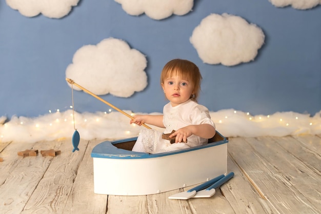 Une enfant fille est assise dans un bateau avec une canne à pêche et un poisson sur fond de nuages blancs