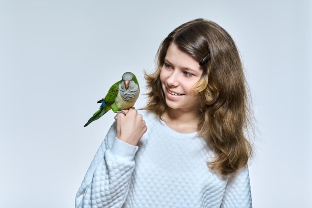 Enfant fille avec perroquet quaker vert pour animaux de compagnie regardant la caméra sur fond de studio clair