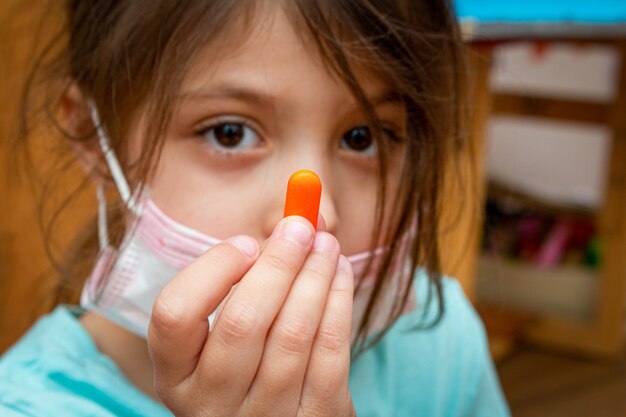 Photo enfant fille portant un masque de protection médical avec une pilule dans une main à la maison pendant l'isolement en quarantaine