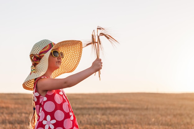 Enfant fille en robe chapeau de paille dans un champ de blé Enfant souriant dans des lunettes de soleil coucher de soleil campagne esthétique de style Cottagecore