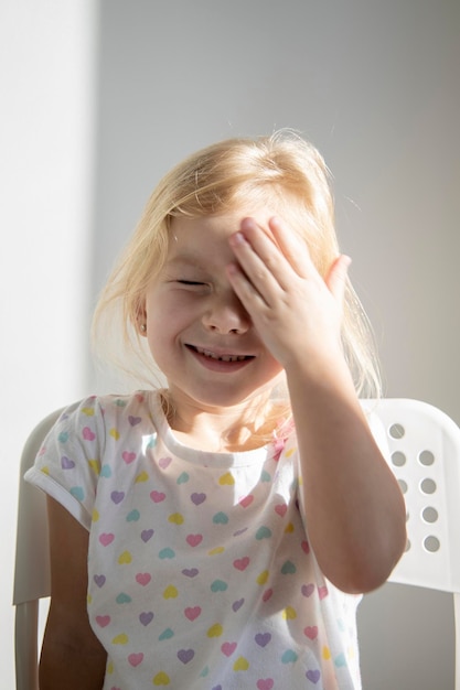 Enfant fille souriante blonde aux yeux fermés ferme les yeux avec sa paume sous les rayons du soleil