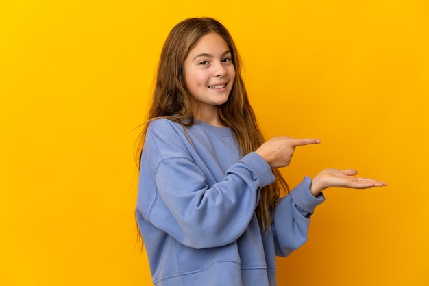 Enfant sur fond jaune isolé holding copyspace imaginaire sur la paume pour insérer une annonce