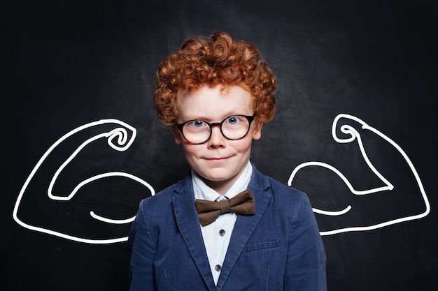 Enfant fort en cravate à papillon et lunettes de costume bleu sur fond de tableau noir