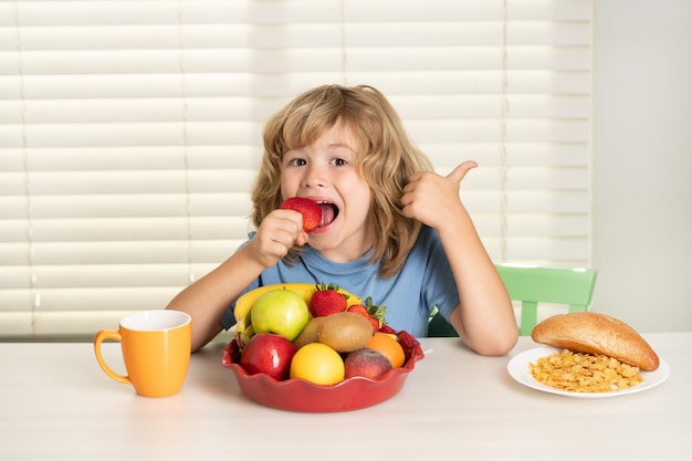 Enfant avec fraise fruits d'été enfant préadolescent dans la cuisine à la table mangeant des légumes et