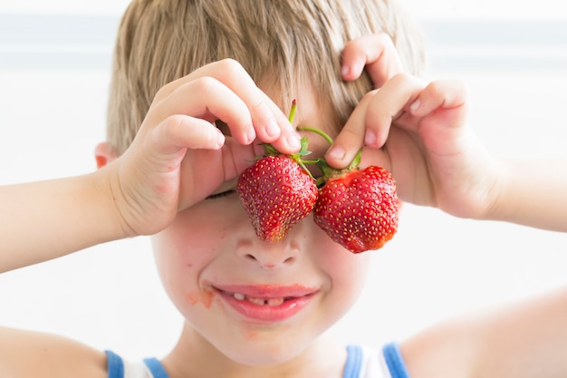 Un enfant avec des fraises. Le garçon tient deux fruits rouges près des yeux
