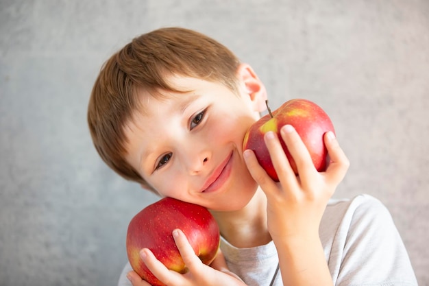 Enfant avec des fruits Un garçon drôle tient de grosses pommes rouges