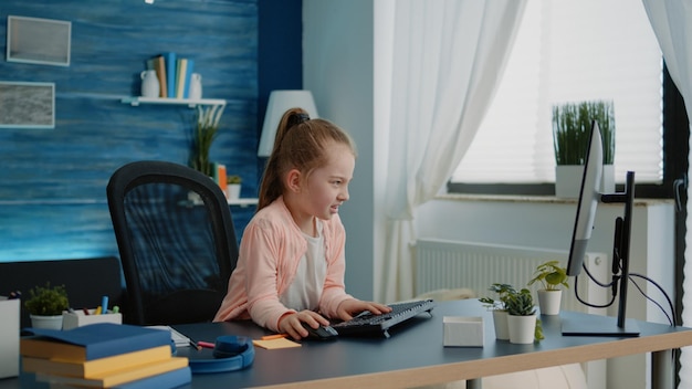 Enfant frustré utilisant un ordinateur et un clavier pour faire ses devoirs à la maison. Petite fille regardant un moniteur pour un cours en ligne sur une connexion Internet pour un enseignement à distance. Enfant de l'école primaire