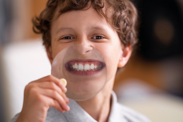 Enfant gai avec des lunettes montre des dents blanches dans le verre d'une grande loupe