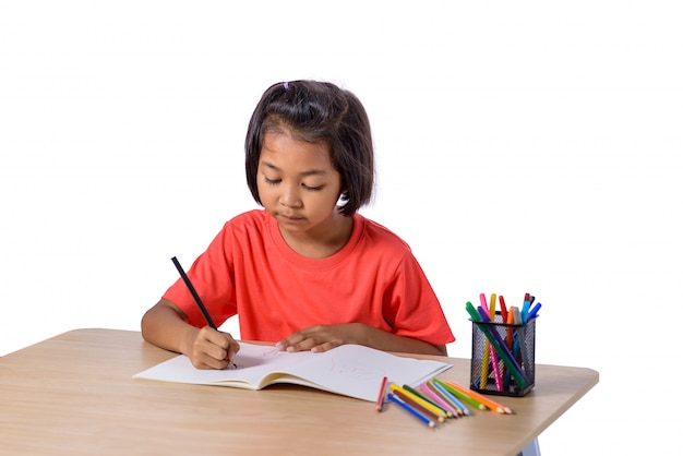 Enfant gai mignon, dessin à l'aide d'un crayon de couleur assis à une table isolée sur fond blanc