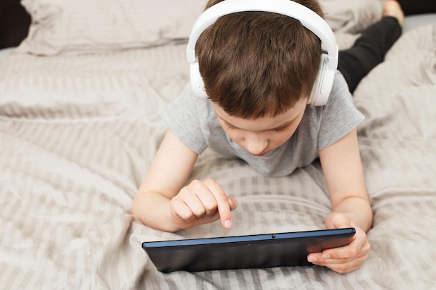 Enfant garçon allongé sur le lit avec tablette pc avec casque sans fil