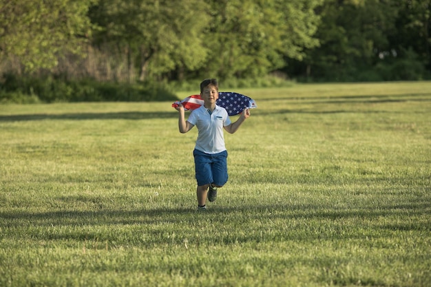 Enfant garçon célébrant le 4 juillet Jour de l'Indépendance des États-Unis Enfant courant avec le symbole du drapeau américain des États-Unis sur un champ de blé