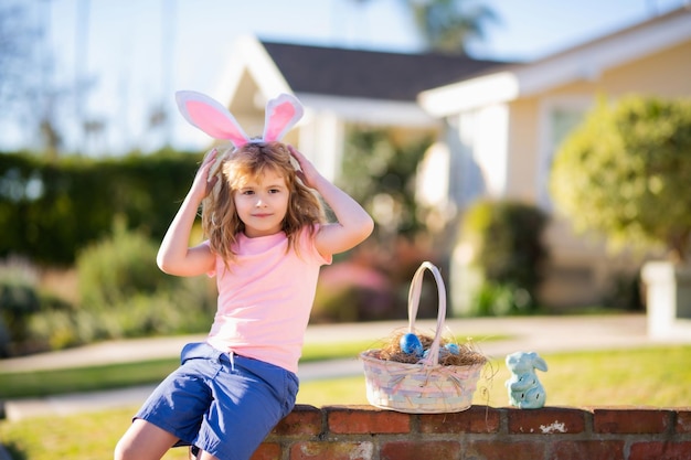 Enfant garçon chassant les oeufs de pâques Enfant avec des oeufs de pâques et des oreilles de lapin en plein air Activité pour enfants pour Pâques dans la nature